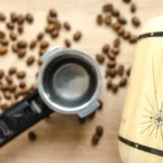 Green coffee beans spilling from a glass jar on a wooden table with steam rising from a nearby roaster.