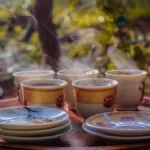 A steaming green tea cup on a bamboo tray with paper lanterns casting soft light and shadows on a journal.
