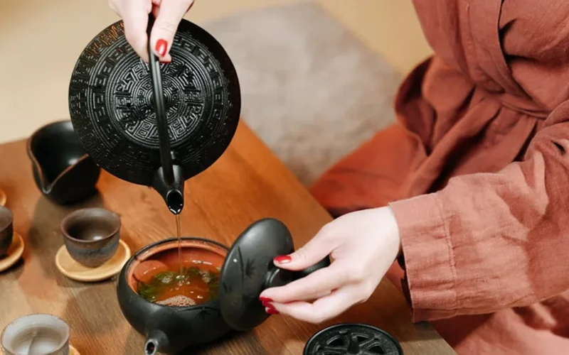 Woman pours tea into ceramic cup in a garden setting with soft natural lighting.
