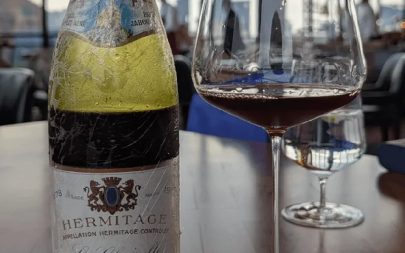 Aged wine bottle on wooden table under golden light with vintage glass nearby.