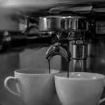 A steaming dark espresso cup in a traditional Italian café with sunlight reflecting on bar tools.