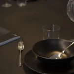 Two glasses of red wine beside an open book on a dark dining table.