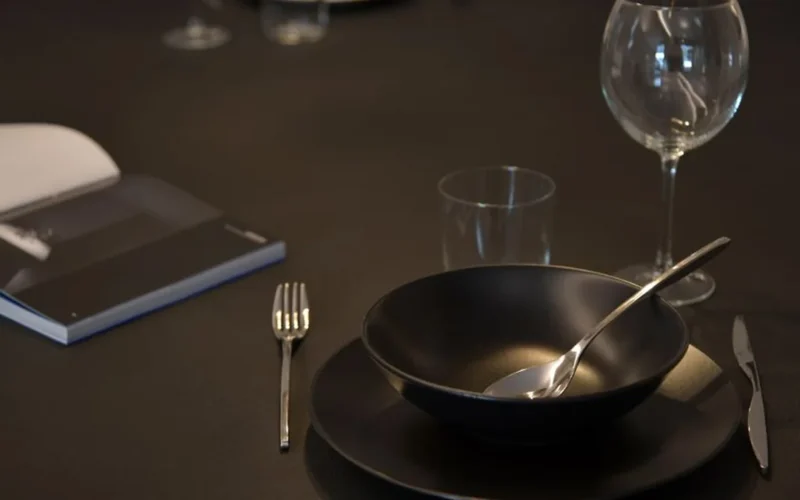 Two glasses of red wine beside an open book on a dark dining table.