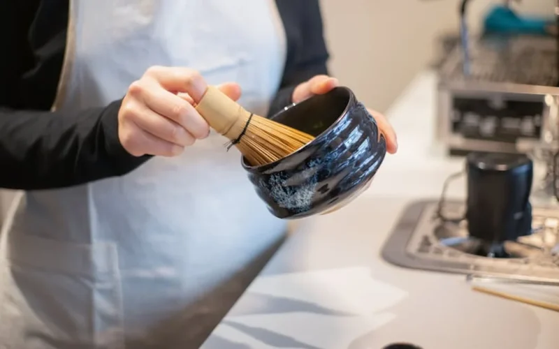 A steaming matcha cup with steam rising, illuminated by paper lanterns casting soft shadows on a wooden table.