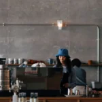 A professional barista serving a cup of specialty coffee with a warm smile in a cafe setting.