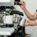 A modern espresso machine pouring dark coffee into a black cup with steam rising in a minimalist kitchen.