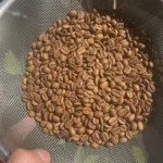 Golden coffee beans roasting in microwave with steam rising from glass bowl on wooden table.