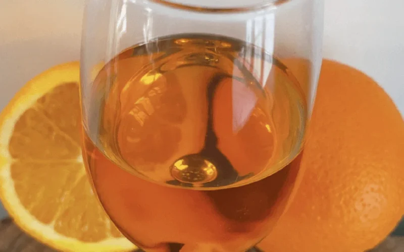 A close up of cloudy orange wine in a glass on a dark wooden table.