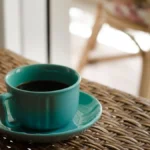 A ceramic coffee cup on a wooden cafe table with natural morning sunlight.