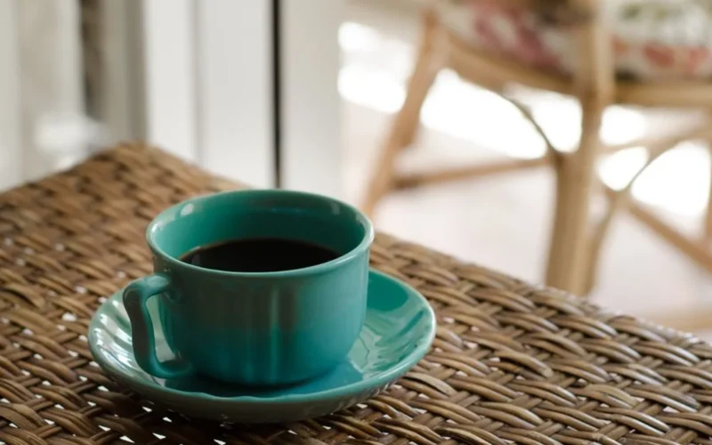 A ceramic coffee cup on a wooden cafe table with natural morning sunlight.