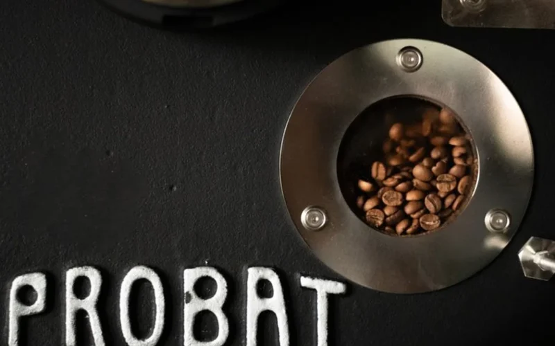 Close-up of a person performing preventive maintenance on an industrial coffee roasting machine drum.