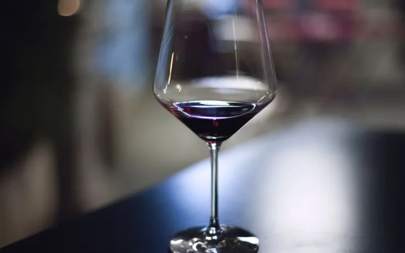 Deep red Bordeaux wine in a crystal glass on a dark wooden surface.