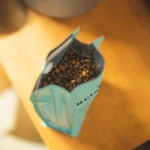 Whole roasted specialty coffee beans spilling from a sealed bag with a one-way valve.