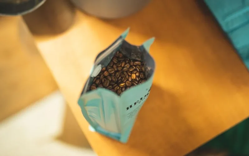 Whole roasted specialty coffee beans spilling from a sealed bag with a one-way valve.