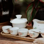 Porcelain teapot with steaming TieGuanYin leaves under warm lighting.