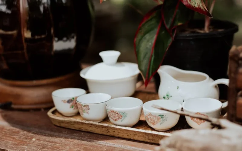 Porcelain teapot with steaming TieGuanYin leaves under warm lighting.