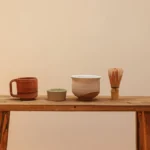 A traditional tea ceremony with matcha powder being poured into a bowl, surrounded by bamboo and fresh tea leaves.