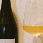 A chilled glass of Chardonnay resting on an oak barrel in a sunlit cellar.