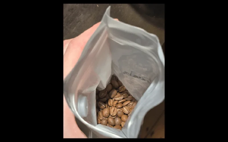 Close-up shot of fresh roasted coffee beans falling from a metal roaster tray.