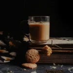 A steaming cup of dark black tea resting on a wooden office desk next to a notebook.