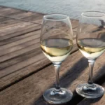 A glass of golden white wine with dried apricots and herbal tea leaves on wood.