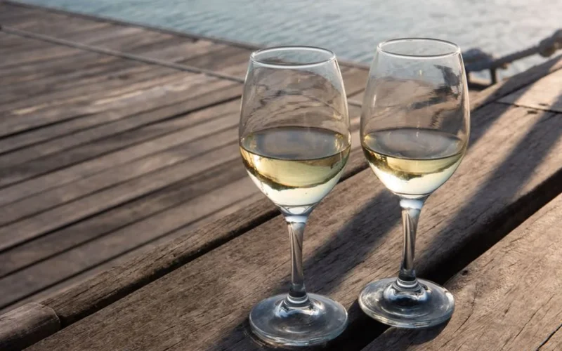 A glass of golden white wine with dried apricots and herbal tea leaves on wood.