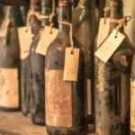 Dusty wine bottles stored on wooden shelves inside a historic stone cellar vault.