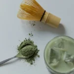 Layered iced matcha latte with botanical garnishes on a marble cafe table.