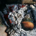 Dried oolong tea leaves being roasted over glowing hot charcoal embers with rising smoke.