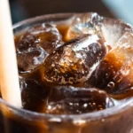 Cold brew coffee in a glass carafe next to whole coffee beans on wood.
