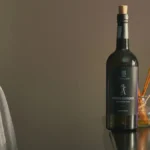 A chilled bottle of Chardonnay and a glass of white wine on wood.