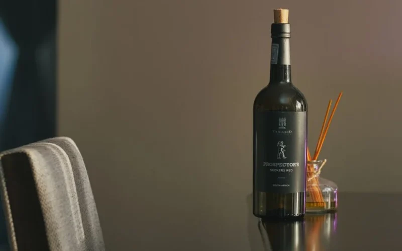 A chilled bottle of Chardonnay and a glass of white wine on wood.