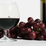 Deep red wine being aerated in a glass decanter on a dark wooden surface.