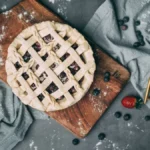 A glass of red wine with fresh blueberries and cherries on a slate background.