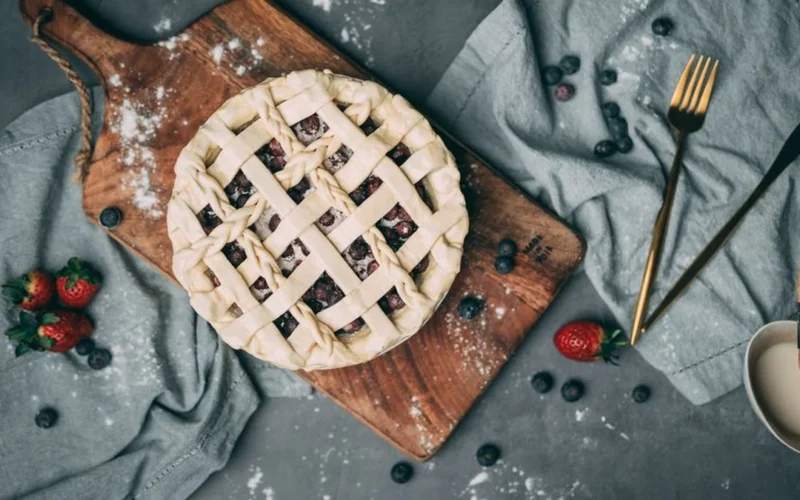 A glass of red wine with fresh blueberries and cherries on a slate background.