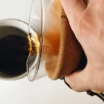 Coffee dripping through a white paper filter into a glass carafe in morning light.