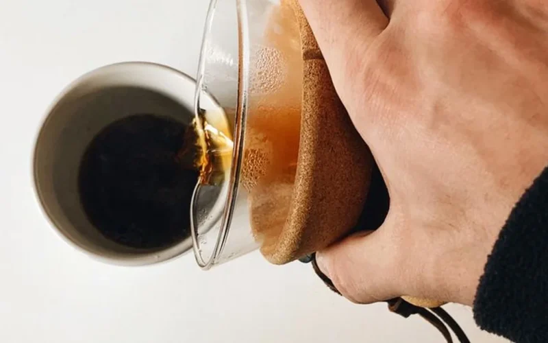 Coffee dripping through a white paper filter into a glass carafe in morning light.