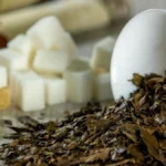Close up of dark roasted oolong tea leaves and amber brewed tea in ceramic cups.