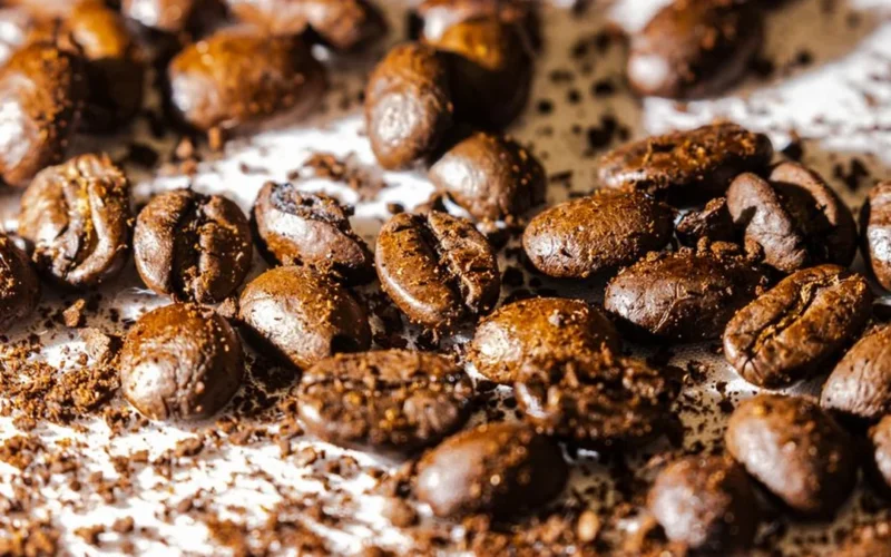 Roasted specialty coffee beans beside white nutritional supplement powder on a dark textured background.