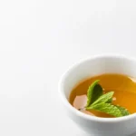 A steaming cup of unsweetened green tea with loose tea leaves on a stone tabletop.