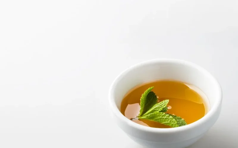 A steaming cup of unsweetened green tea with loose tea leaves on a stone tabletop.