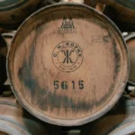 Amber bourbon in a crystal glass resting on a rustic wooden barrel surface.