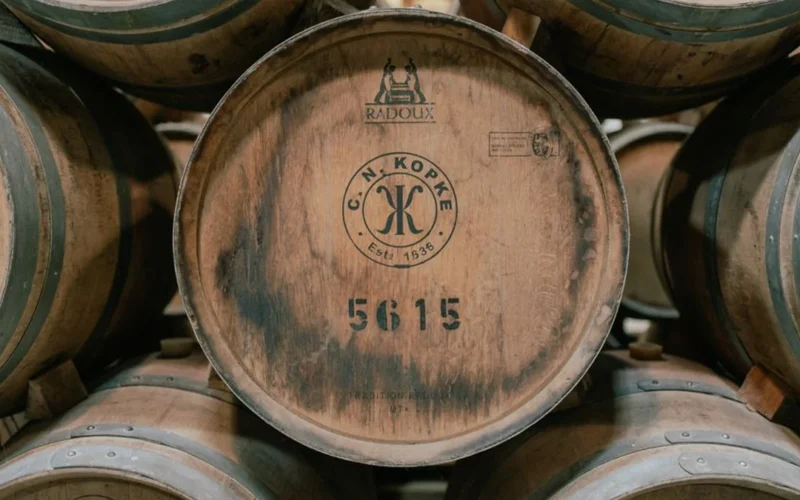 Amber bourbon in a crystal glass resting on a rustic wooden barrel surface.