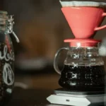 Three clear glass carafes of brewed coffee arranged next to small single origin coffee bean bags.