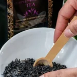 Various loose leaf teas, hibiscus petals, and ginger slices arranged near ceramic cups.