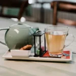 A dark cup of coffee beside a clear glass of green tea on wood.