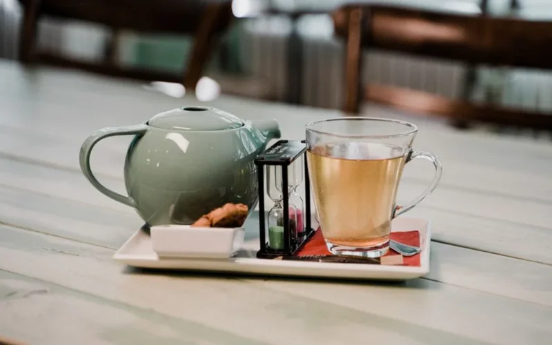 A dark cup of coffee beside a clear glass of green tea on wood.