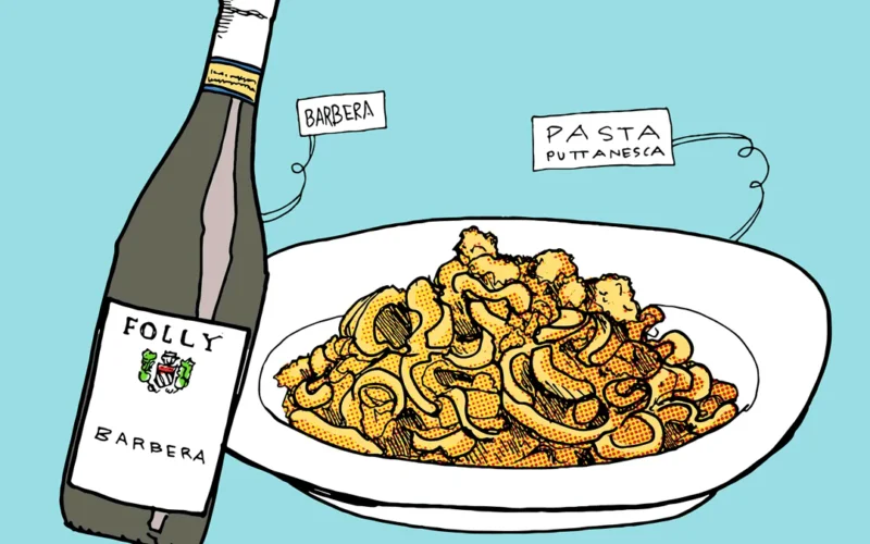 A bowl of savory tomato pasta paired with a glass of red wine on a wooden table.