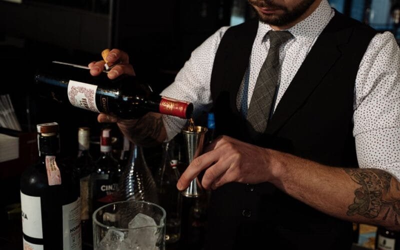 Bottles of vermouth and a botanical cocktail on a marble bar surface.