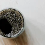 Steam rising from black coffee in a ceramic mug next to an espresso machine.